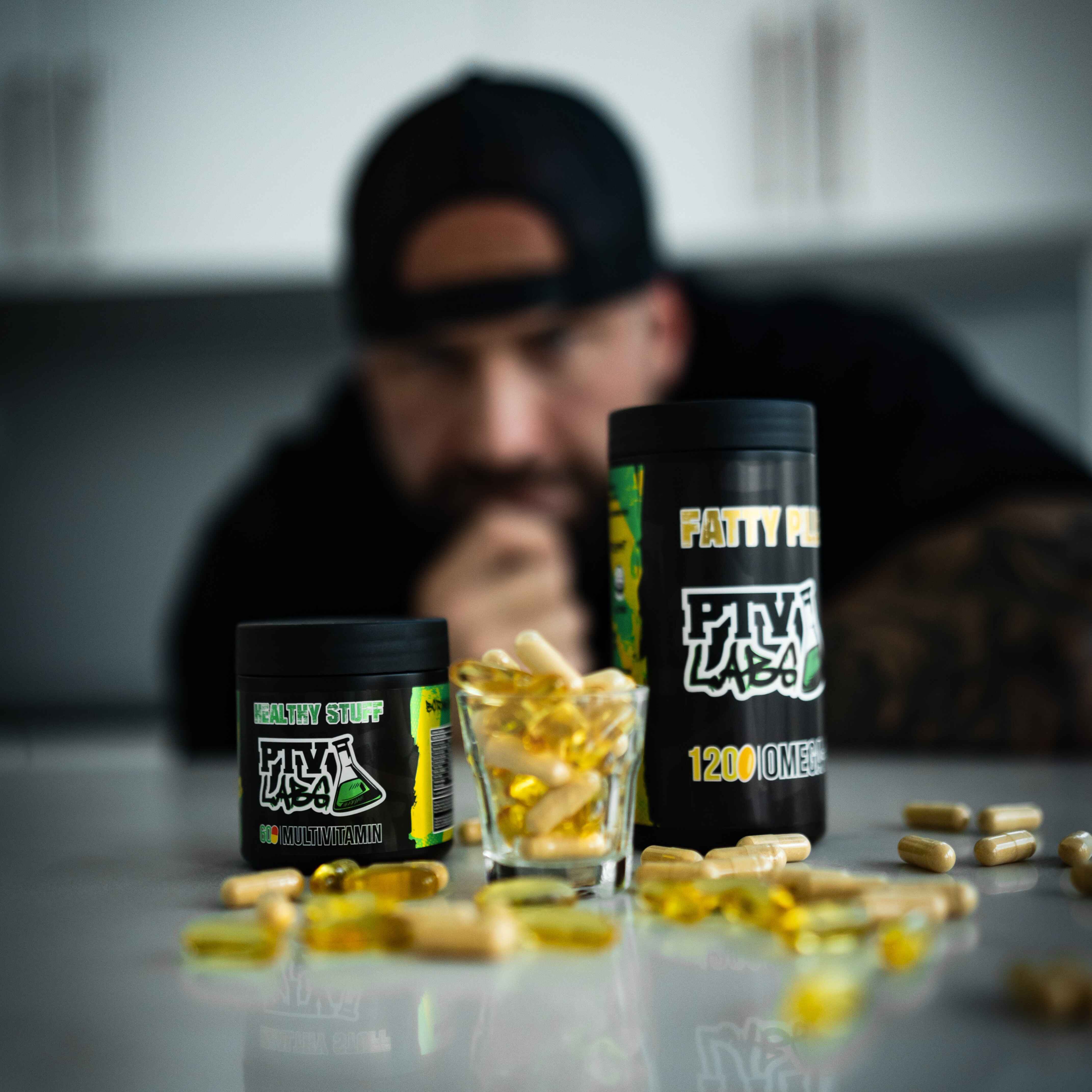 PTVLABS Omega-3 ja monivitamiinilisät kapseleina pöydällä, taustalla mies katsomassa tuotteita.