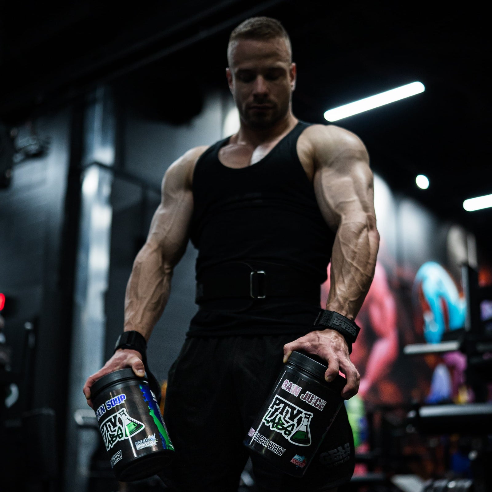 Urheilija kuntosalilla pitelemässä heraproteiinijauheita. Gain Soup ja Gain Juice, laadukkaat heraproteiinit treenin tueksi